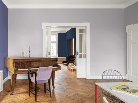 Elegantes fliederfarbenes Wohnzimmer-Interieur mit Flügel, Fischgrätenboden und Türen zum Nebenzimmer
