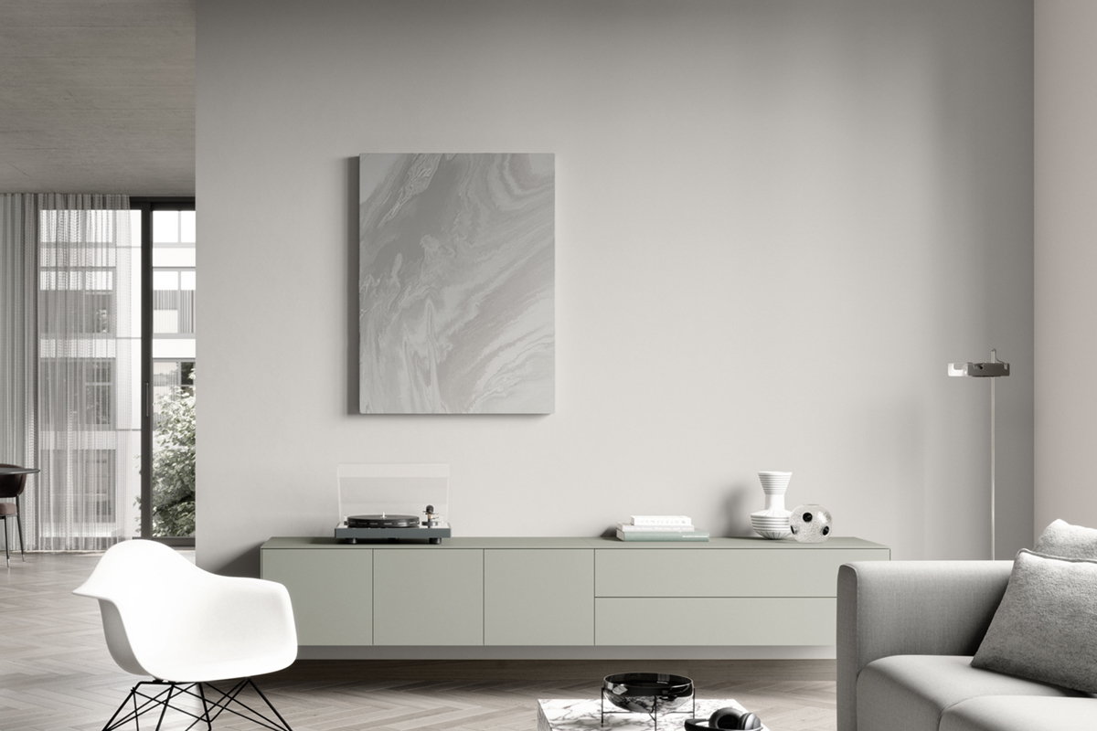 Ausgegrautes Wohnzimmer mit Sofabereich, Sideboard und Fenstern.